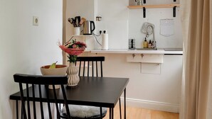 Cucina compatta con mobili bianchi, un piano di lavoro in legno e un piccolo lavello. C'è un tavolo da pranzo con due sedie e un vaso con fiori.