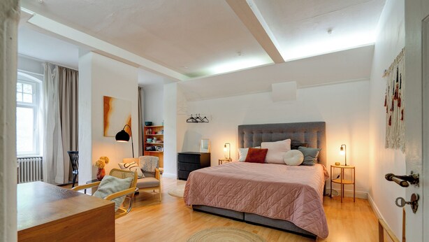 Una camera da letto moderna con un letto grande, una scrivania e una sedia. Si vede una libreria e una finestra con tende.
