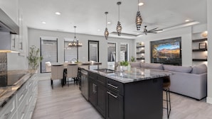 A modern kitchen with a large island, dark cabinetry, and pendant lighting.