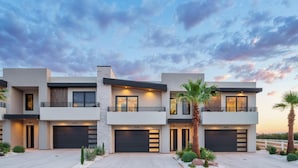 A modern multi-story residential building with two garages, balconies, and a landscaped driveway.