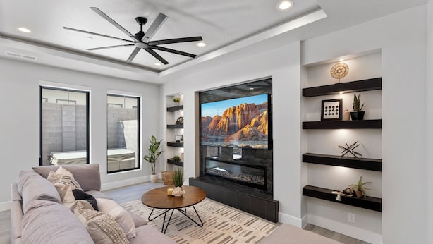 A modern living room with a large flat-screen TV, a ceiling fan, and built-in shelves with decorative items.