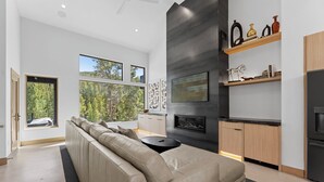 Una sala de estar moderna con un sofá seccional color beige, una chimenea y una cocina con armarios de madera y una encimera negra.