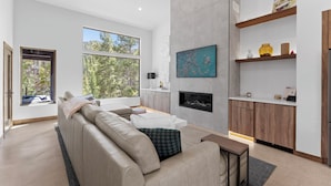 Ein modernes Wohnzimmer mit einem beigen Sofa, einem Kamin und einer Küchenzeile mit Holzausbau und Arbeitsplatte.