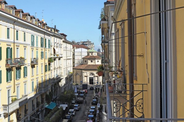 A narrow street with buildings on either side, a church with a green roof, and parked cars.