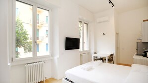 Un dormitori amb un llit, escriptori, cadira, televisió i finestra.