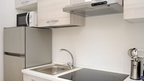 Cuina compacta amb microones integrat, nevera d'acer inoxidable, rentatge amb un aixeta moderna i fogó d'inducció negre.