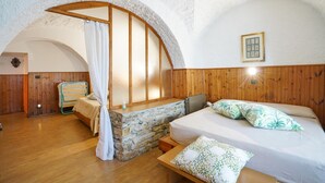 A cozy bedroom with a stone bench, a bed with floral pillows, and a wooden headboard. - Amazing apartment in Costarainera (Costarainera)