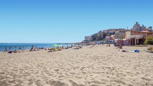 A beach with people sunbathing and swimming, buildings in the background, and clear skies. - Amazing apartment in Costarainera (Costarainera)