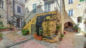 A courtyard with a stone building, a yellow staircase, and potted plants. - Amazing apartment in Costarainera (Costarainera)