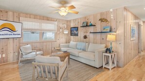 A beach-themed living room with a sofa, chairs, a small table, and a ceiling fan.