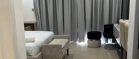 A modern hotel room with a bed, a seating area, a small table, and a television.