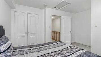 A bedroom with a bed, two white doors, a ceiling vent, and a wooden railing in the background.