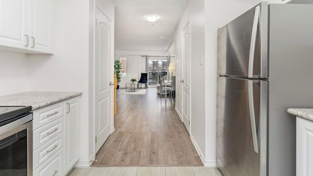 Una cocina moderna con armarios blancos, un refrigerador de acero inoxidable y piso de madera.