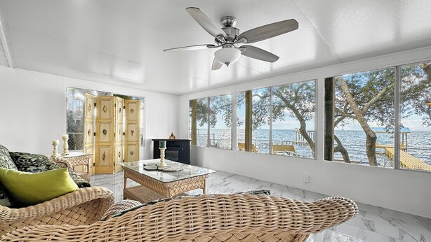 A spacious room with a large window offering a view of the sea, wicker furniture, and a ceiling fan. - Baywatch Waterfront Paradice  8 m to bch, private pier, Sleeps 8 Fenced Dog Area (Gulf Shores)