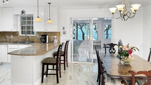 A kitchen with a large island, white cabinets, and a dining area with a table and chairs. - Baywatch Waterfront Paradice  8 m to bch, private pier, Sleeps 8 Fenced Dog Area (Gulf Shores)
