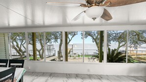 A spacious room with a large bay window overlooking a beach, a ceiling fan, and a marble floor. - Baywatch Waterfront Paradice  8 m to bch, private pier, Sleeps 8 Fenced Dog Area (Gulf Shores)