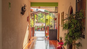 A hallway with a tiled floor leading to a covered outdoor area with plants and a gate. - Casa San Jeronimo (San Pedro Mixtepec)