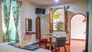 A hotel room with a bed, a small table with a chair, a TV mounted on the wall, and a window with curtains. - Casa San Jeronimo (San Pedro Mixtepec)