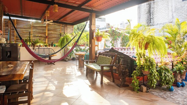 A covered patio area with a wooden table and chairs, a hammock, and various potted plants. - Casa San Jeronimo (San Pedro Mixtepec)