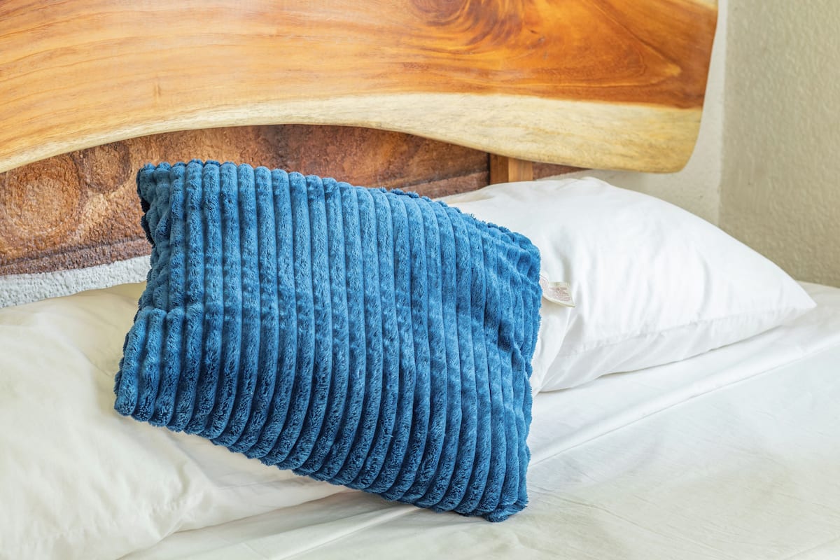 A bed with a wooden headboard, a white pillow, and a blue textured pillow.
