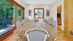 A dining room with a long wooden table and patterned chairs, large windows, and framed artwork on the walls. - Sea Breeze Dream | Water View, Rooftop Deck, Game Room, Fire Pit & Cozy Backyard! (San Diego)