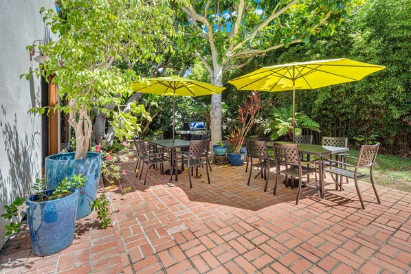 A patio with brick flooring, outdoor furniture, and yellow umbrellas. - Sea Breeze Dream | Water View, Rooftop Deck, Game Room, Fire Pit & Cozy Backyard! (San Diego)
