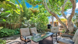 An outdoor patio with a built-in fire feature, surrounded by chairs and lush greenery. - Sea Breeze Dream | Water View, Rooftop Deck, Game Room, Fire Pit & Cozy Backyard! (San Diego)