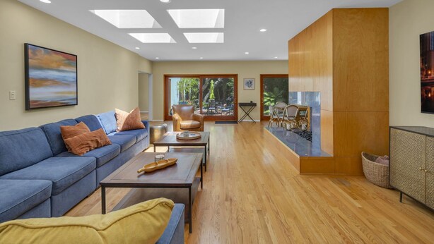 A modern living room with a blue sofa, wooden coffee table, and a view of the outdoors through large windows. - Sea Breeze Dream | Water View, Rooftop Deck, Game Room, Fire Pit & Cozy Backyard! (San Diego)