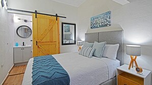 A bedroom with a bed, a nightstand, a wooden door, a mirror, and a wall-mounted artwork. - Estudio Perfecto Ubicación Ideal (La Paz)