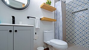 A bathroom with a toilet, a sink, a mirror, and a shower area. - Estudio Perfecto Ubicación Ideal (La Paz)