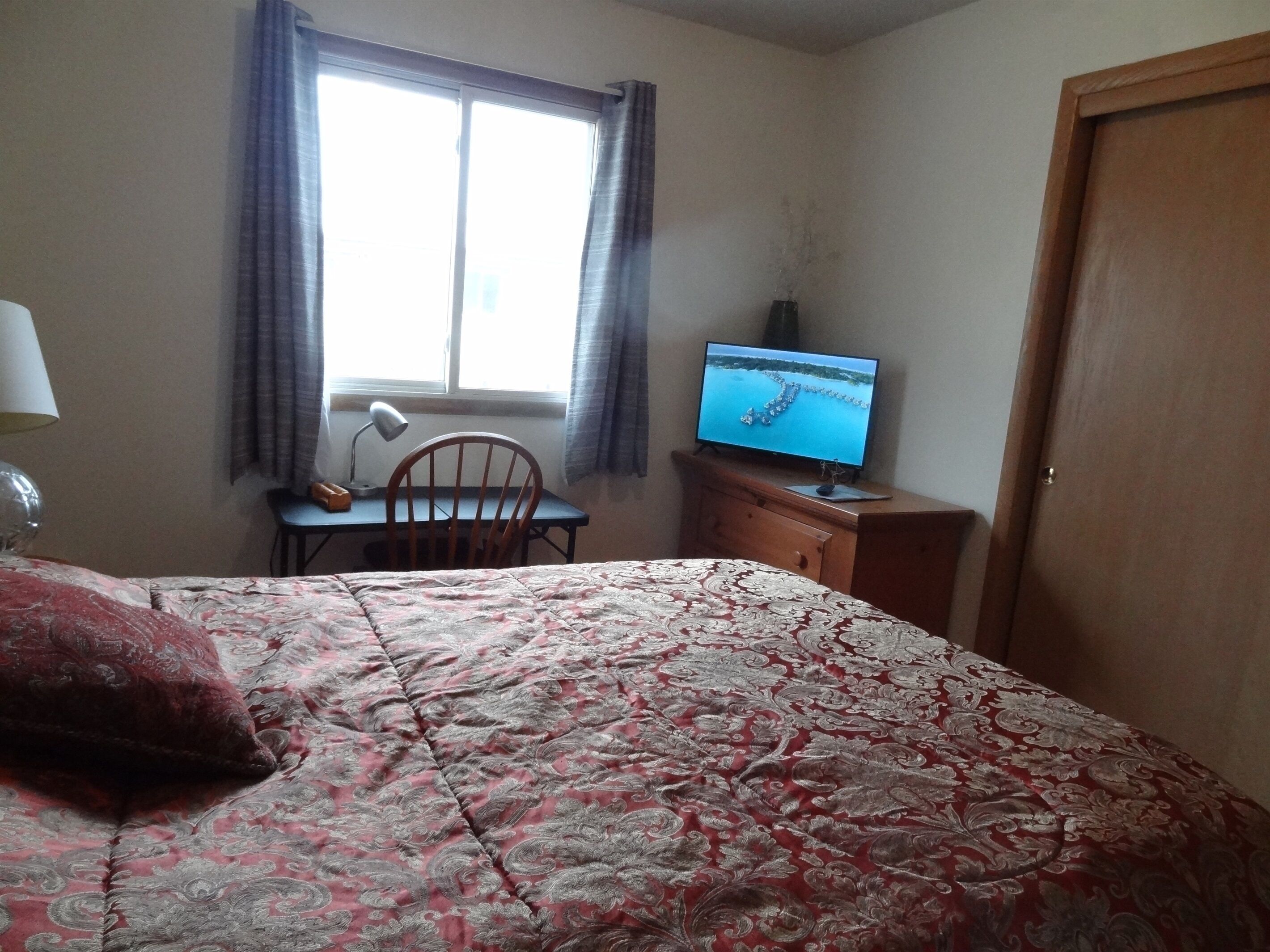 Une chambre d’hôtel avec un lit, un bureau avec un ordinateur, une chaise et une fenêtre avec des rideaux.