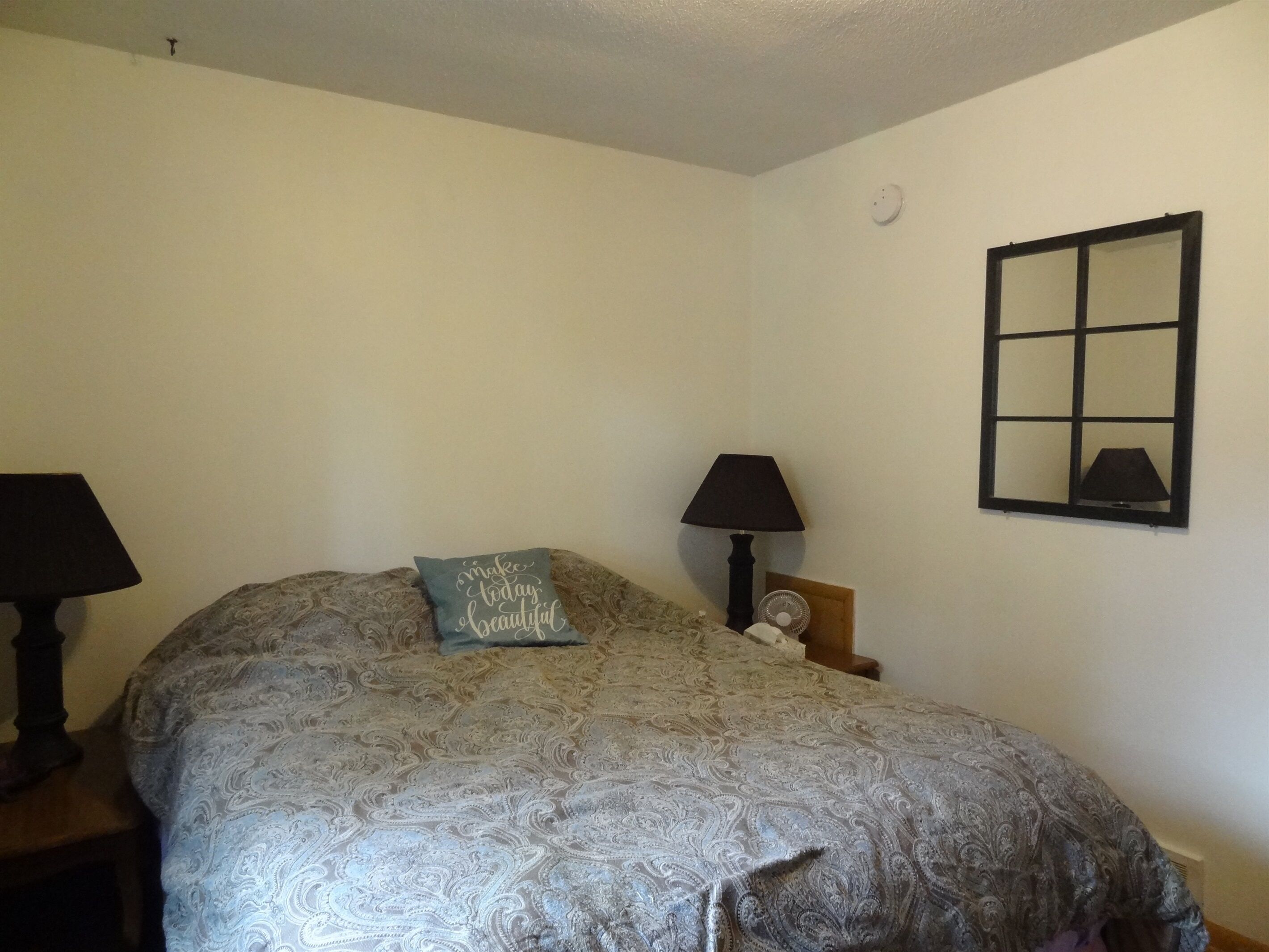 Une chambre à coucher avec un lit, deux tables de chevet, une lampe et un miroir au mur.