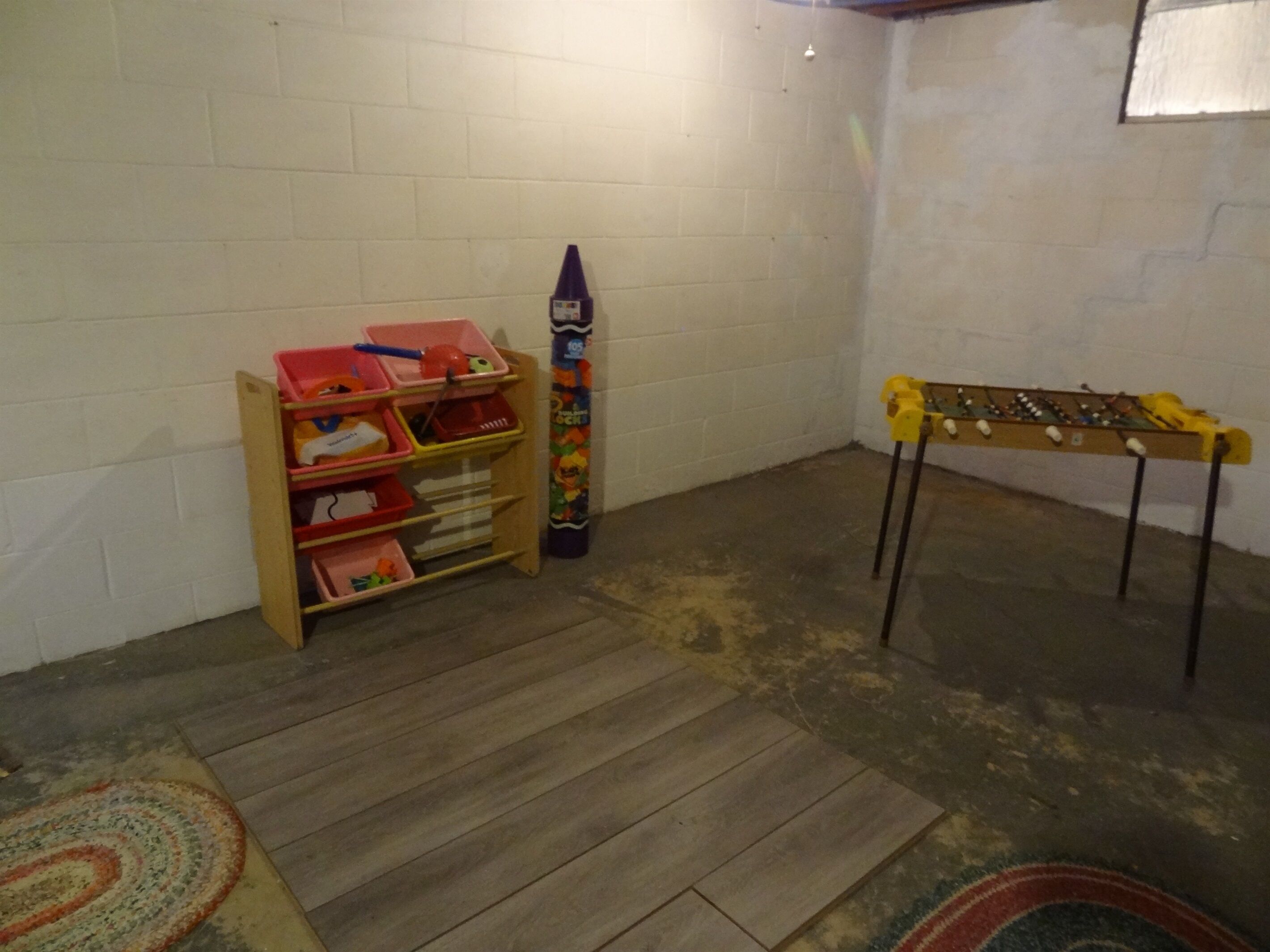 Una habitación con una estantería de madera, una mesa de fútbolín y un mueble de guardado de juguetes de colores.