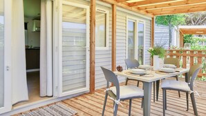 A covered patio with a table set for dining, sliding glass doors leading to a kitchen, and a wooden deck.