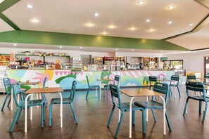 A restaurant with teal chairs and tables, a colorful mural, and various food and drink displays.