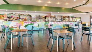 A restaurant with teal chairs and tables, a colorful mural, and various food and drink displays.
