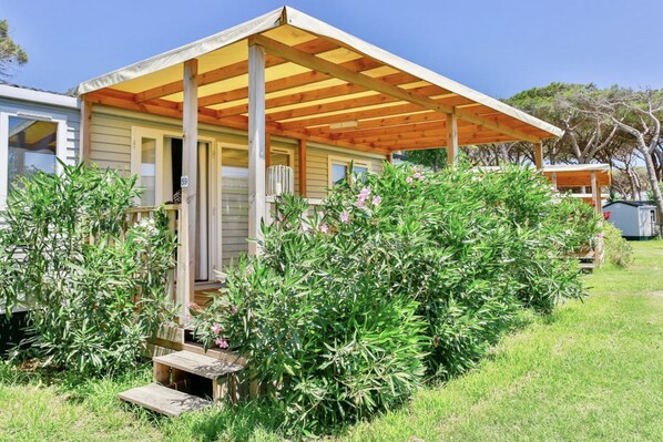 A single-story house with a covered porch, surrounded by lush greenery and a small garden.
