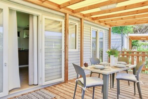 Un patio cubierto con una mesa lista para comer, puertas corredizas de vidrio que dan a una cocina y una terraza de madera.