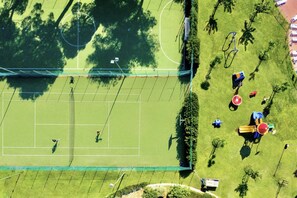 Vista aérea de una cancha de tenis rodeada de árboles y juegos infantiles.