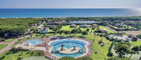 A resort with multiple swimming pools, a large central pool, and a view of the sea.