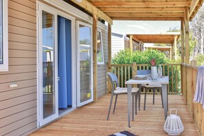 A covered outdoor patio with a table and chairs, a sliding glass door, and a wooden deck.