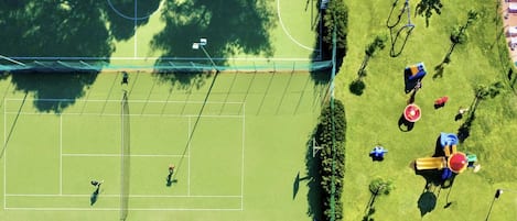 Vista aérea de una cancha de tenis rodeada de árboles y juegos infantiles.