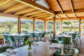 Un espacio de comedor al aire libre con vigas de madera, sillas verdes y mesas dispuestas para comer.