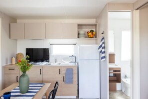 Cocina pequeña con estufa a gas, lavamanos y refrigerador blanco. Hay una mesa de comedor con un florero y una taza azul.