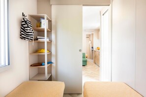 Una habitación pequeña con cama, armario y estante con varios objetos.