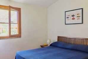 A bedroom with a bed, a nightstand, a lamp, a window, and a framed fish illustration on the wall.