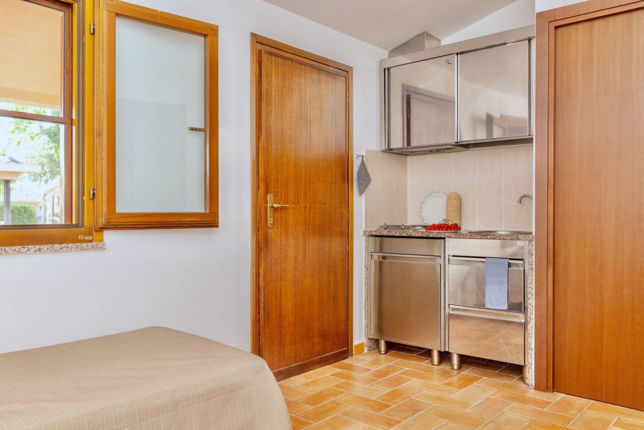 Habitación compacta con cama, kitchenette y puerta de madera.
