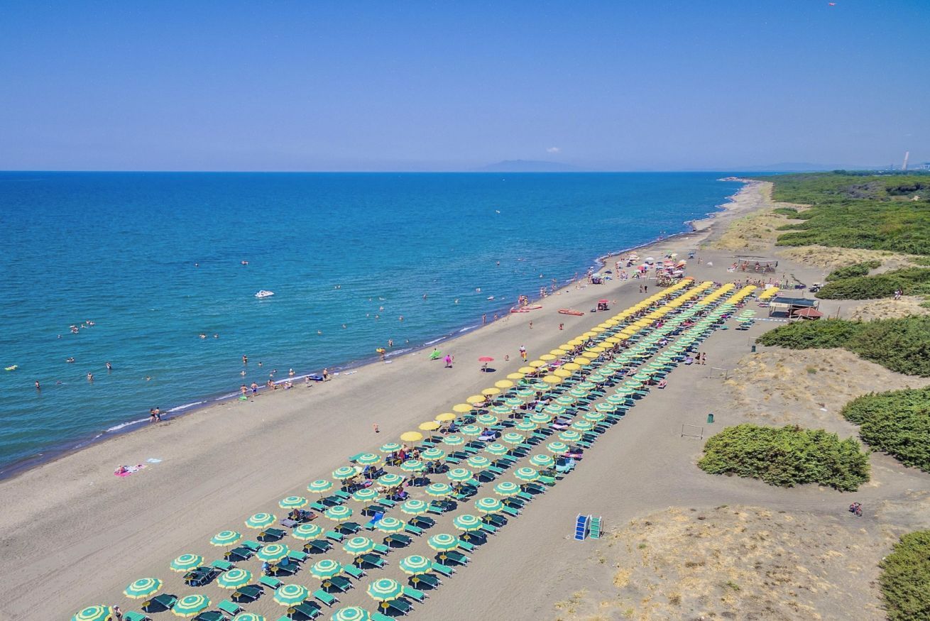 A beach with rows of umbrellas and sun loungers, a clear sky, and the sea.