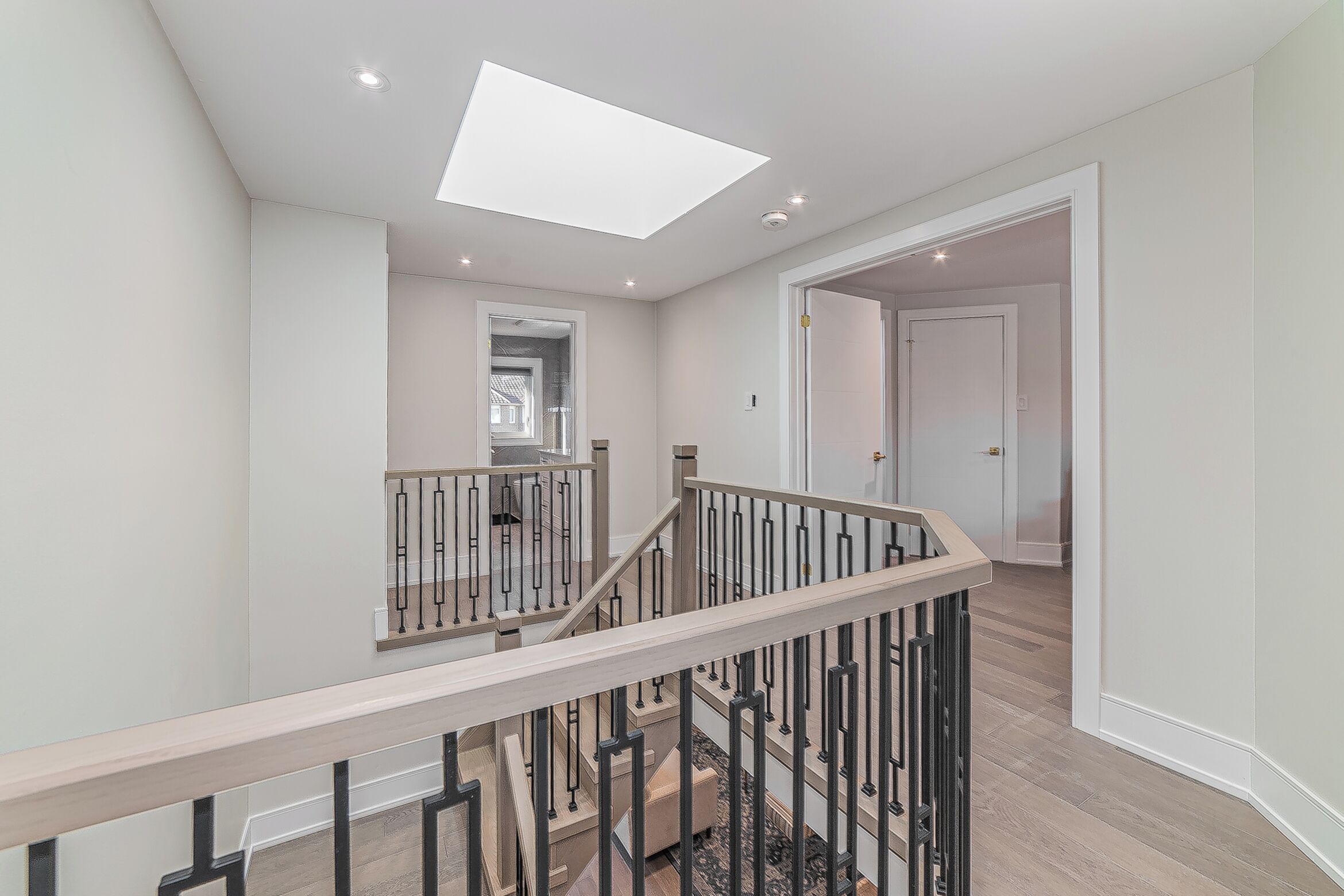 A modern interior with a staircase, a skylight, and a view into another room.