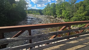 A wooden bridge over a rocky river with lush greenery on both sides. - Valley Home with Game Room, Walking Distance to Narrow Gauge Trails & Restaurant (Carrabassett Valley)